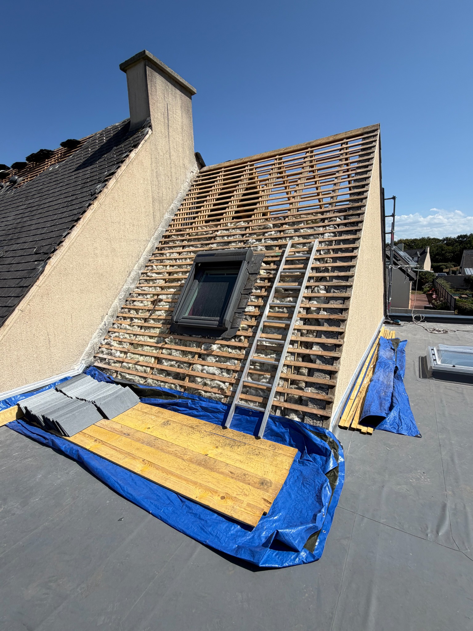 Toiture en cours de travaux avec couverture déposée, liteaux visibles et mur latéral