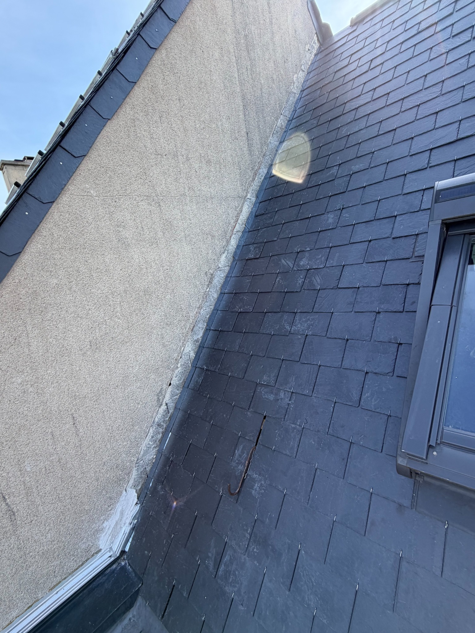 Jonction d’un mur enduit et d’une toiture en ardoises à proximité d’une fenêtre de toit